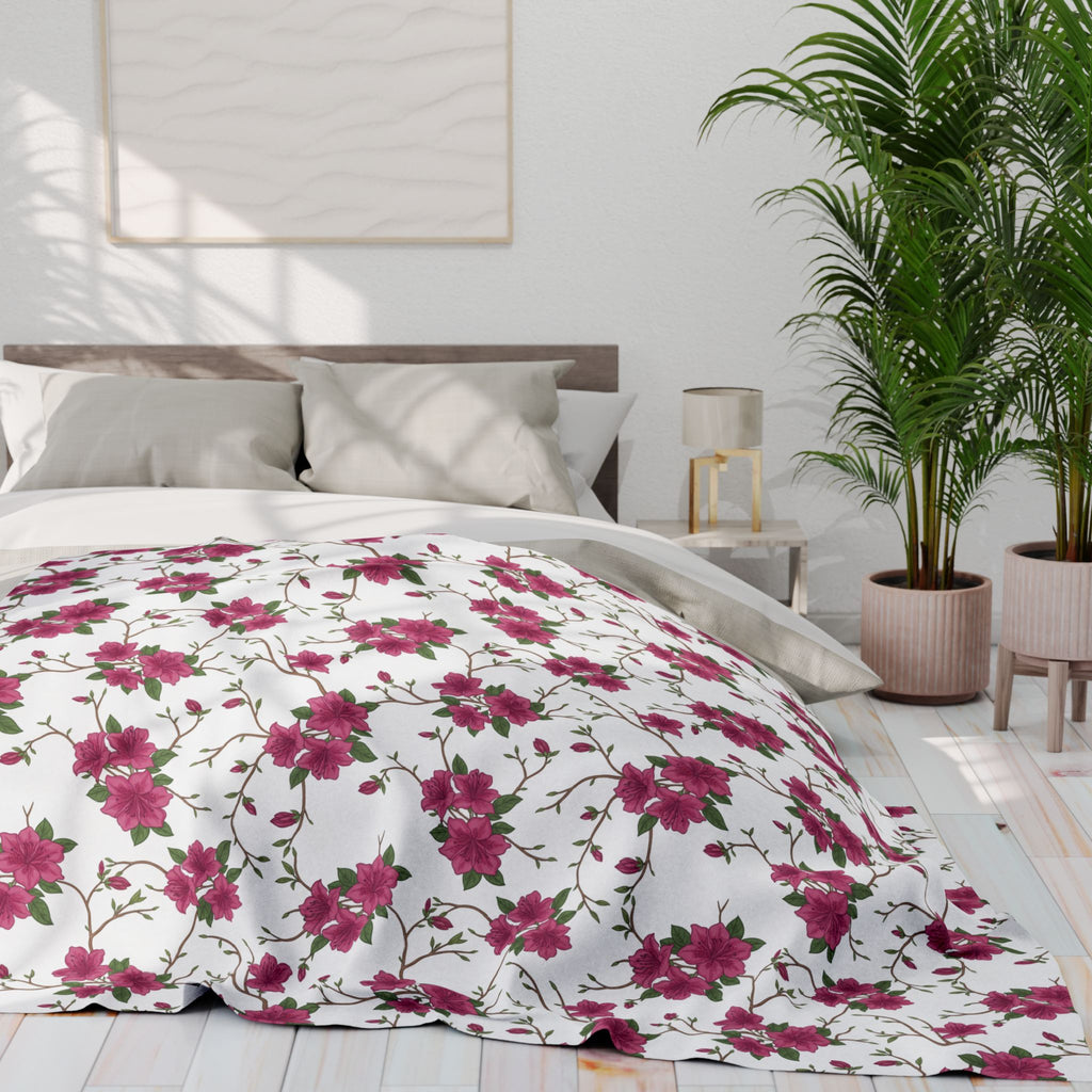 Floral patterned comforter on a bed in a bright bedroom with plants and a lamp.