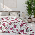 Floral patterned comforter on a bed in a bright bedroom with plants and a lamp.