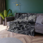 Gray sofa with a decorative gray blanket draped over it in a living room setting.